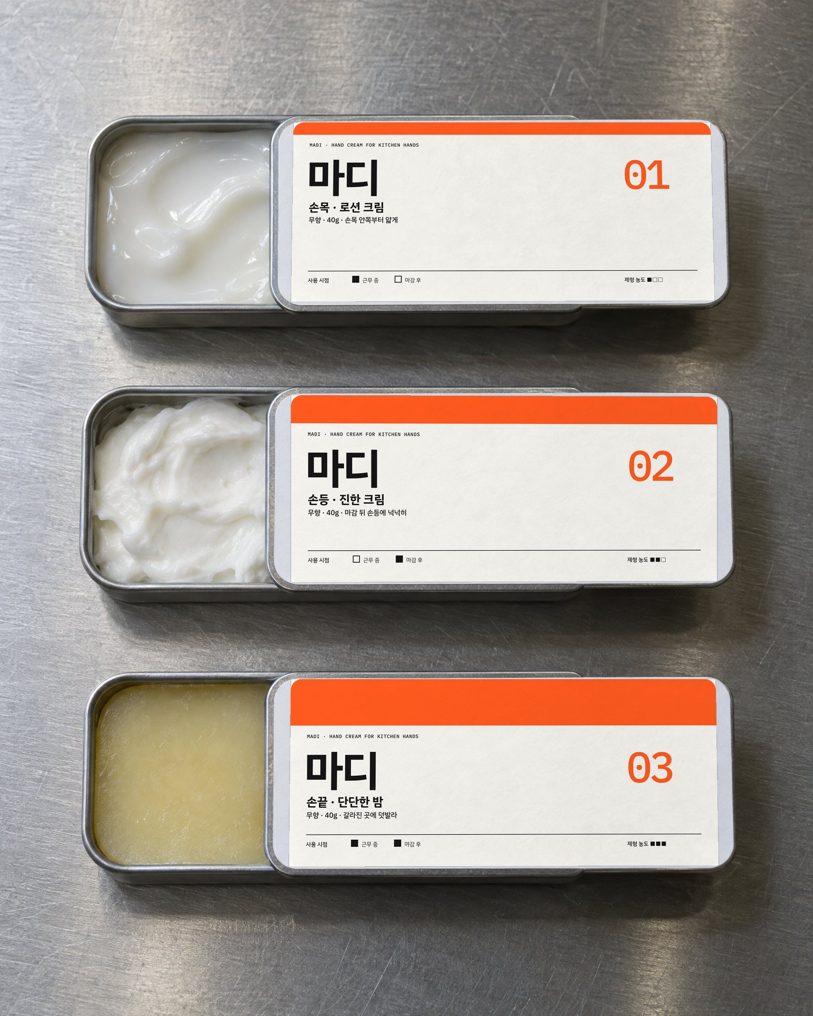 스테인리스 위에 뚜껑을 밀어 연 마디 틴 3종 — 로션·크림·밤과 01·02·03 라벨